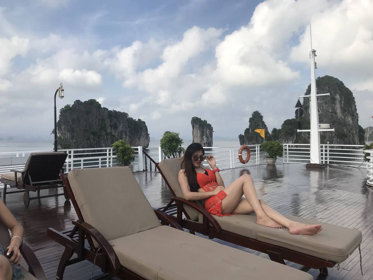 Guest relaxing on an overnight cruise sundeck with limestone karsts behind, Halong Bay
