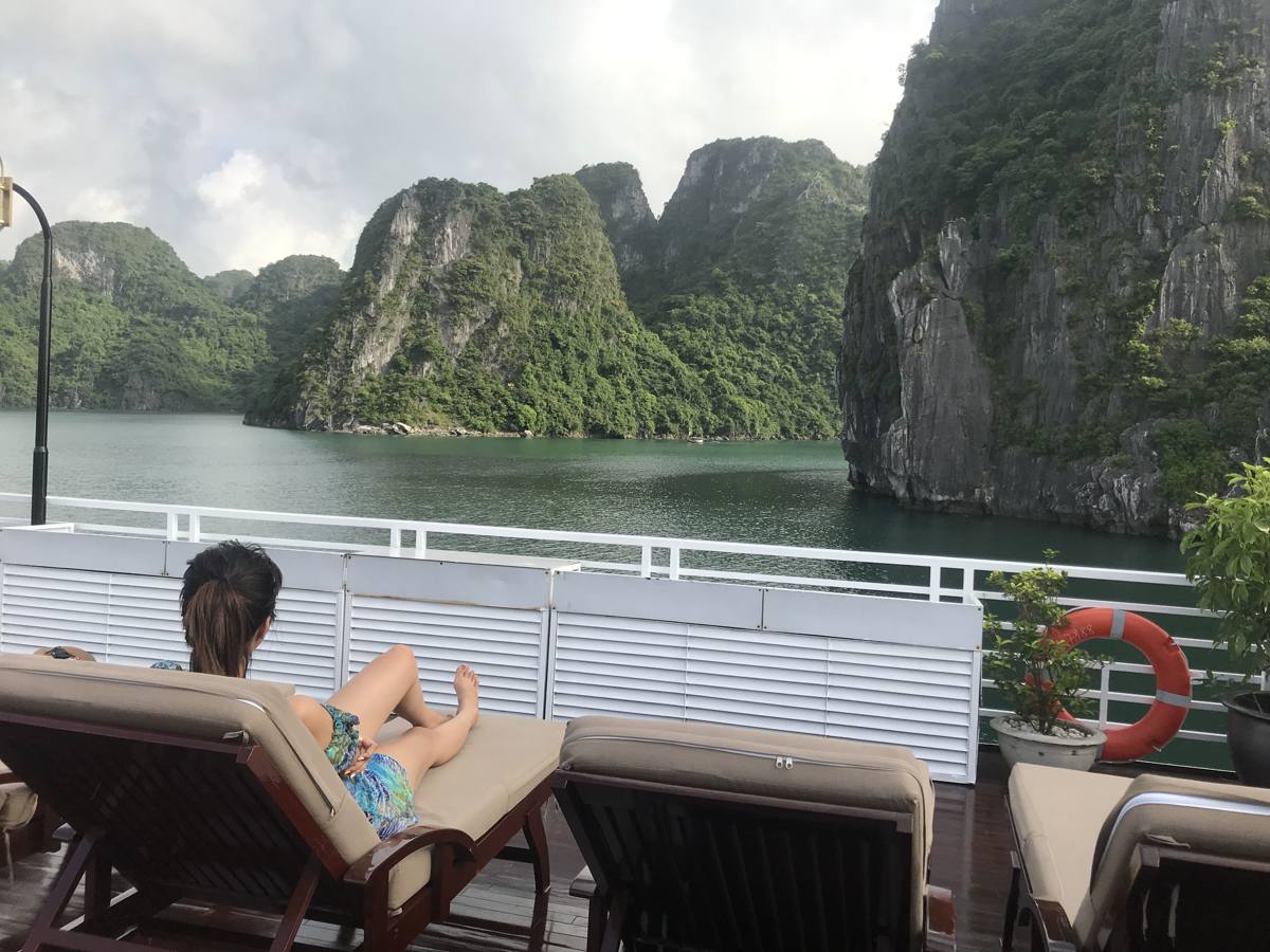 Guest on a cruise sundeck facing limestone cliffs and calm water, Halong Bay